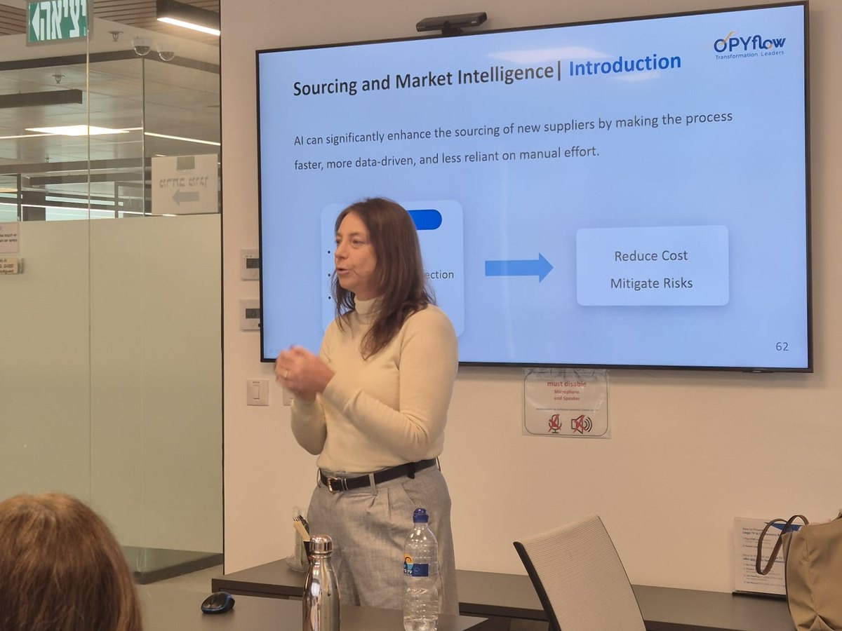 A trainer speaks in front of a slide titled Sourcing and Market Intelligence, which names reducing cost and mitigating risk as the aims.